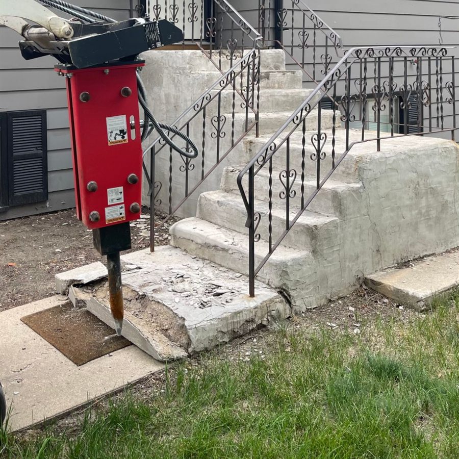 Concrete front stair removal by Demolition King Group: a hydraulic breaker breaking up the bottom step of a house's exterior stairs