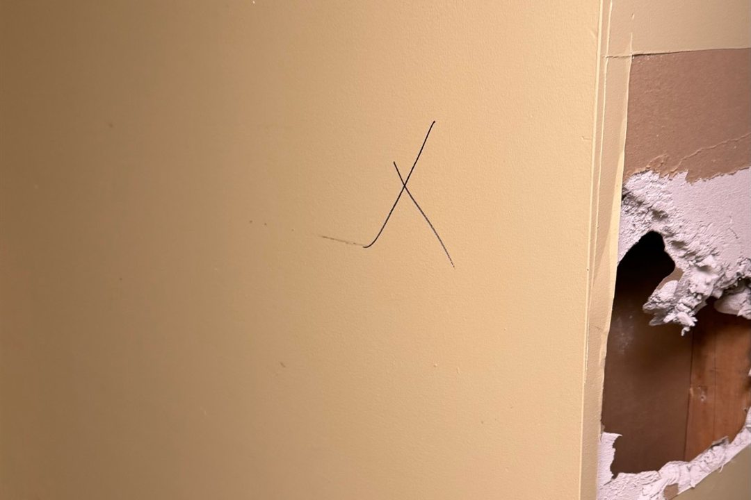 Before an interior gut-out by Demolition King Group: painted drywall wall marked for removal, with an inspection hole cut beside it