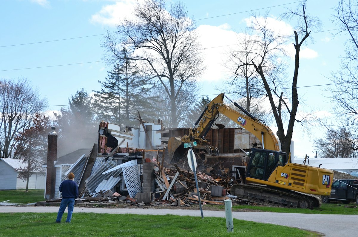 Excavator demolishing a house beside a residential street