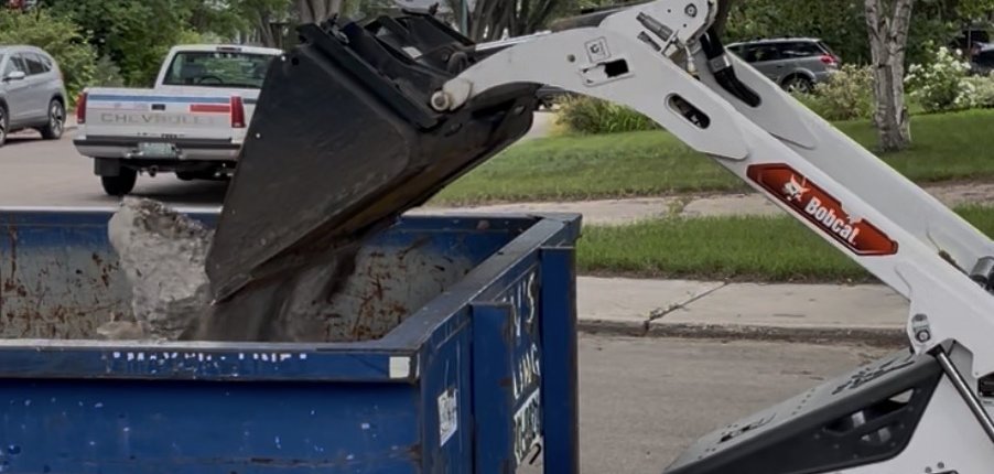 Bobcat compact track loader loading demolition debris into a roll-off bin during site cleanup by Demolition King Group